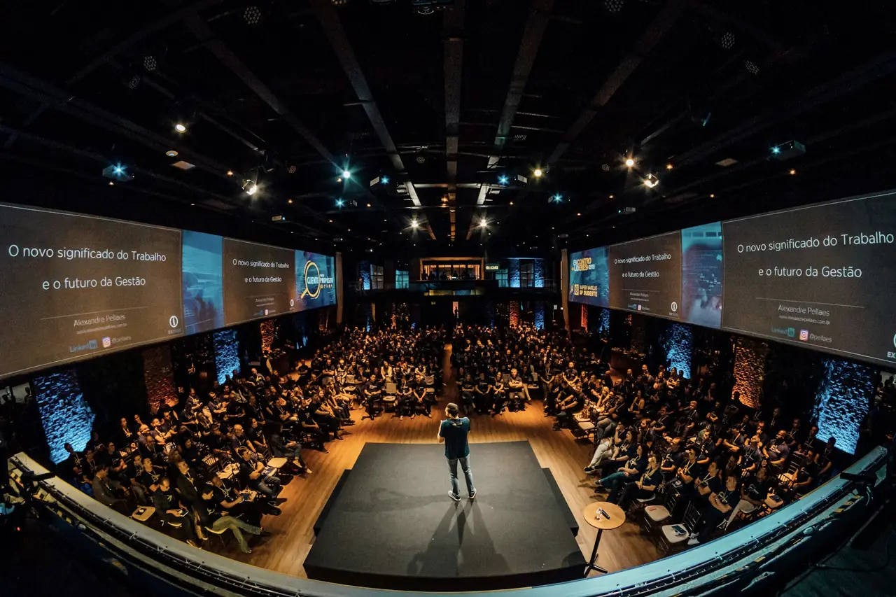 Auditório de evento corporativo com palestrante no palco e plateia